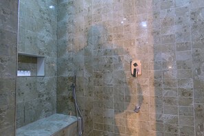 A shower area with a tiled wall, a handheld showerhead, and a wall-mounted control panel. - Arcade Suites (Abuja)