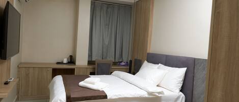 Une chambre d’hôtel moderne avec un lit en bois, un bureau, une chaise, un téléviseur à écran plat et une fenêtre avec des rideaux.