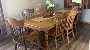 Ein Esszimmer mit Holztisch und -stühlen, einem Deckenventilator und dekorativen Wandbehängen.