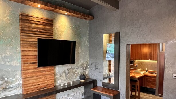 A modern bedroom with a large bed, a flat-screen TV mounted on a textured wall, and a skylight above. - Beautiful studio in Jalatlaco, a beautiful neighborhood (Oaxaca de Juárez)