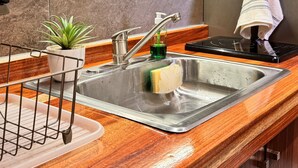 A kitchen with wooden cabinets, a stainless steel sink, a built-in stove, a small potted plant, and a dish rack. - Beautiful studio in Jalatlaco, a beautiful neighborhood (Oaxaca de Juárez)