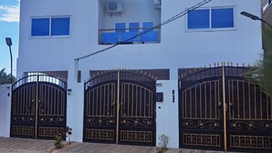 A modern two-story building with a white facade, three large black gates with gold detailing, and a satellite dish on the roof.