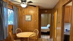 A wooden interior with a dining table and chairs, a ceiling fan, a bed, and a kitchen area.
