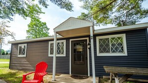 A small, single-story cabin with a dark exterior, a front door, and two windows with diamond-patterned glass.