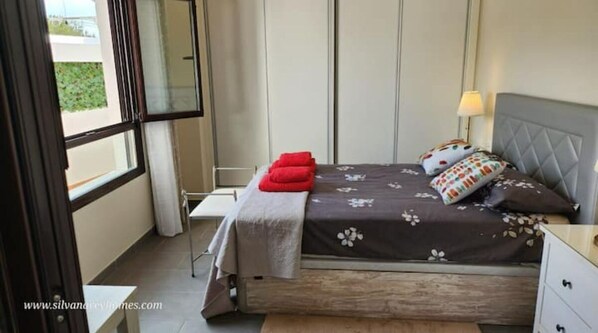 Relax in this serene space with a comfortable bed, bedside table, and window offering a view of lush greenery.