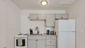 A compact kitchen with white cabinetry, a stove, a sink, and a refrigerator. - Studio Apartment in Winter Haven, FL (Winter Haven)