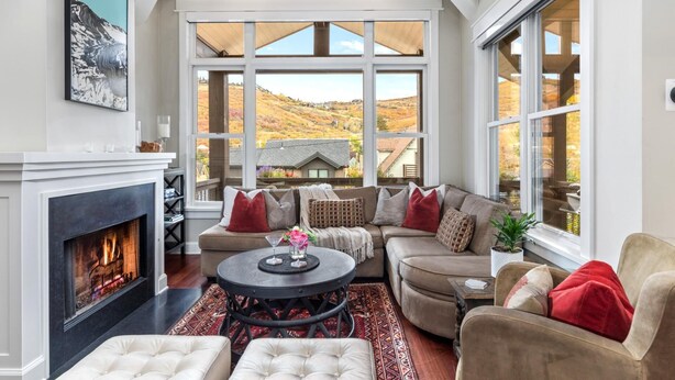 A cozy living room with a fireplace, large windows, and a view of a hillside. - Red Crest 3 Bedrooms PWS-957 by KBM (Park City)
