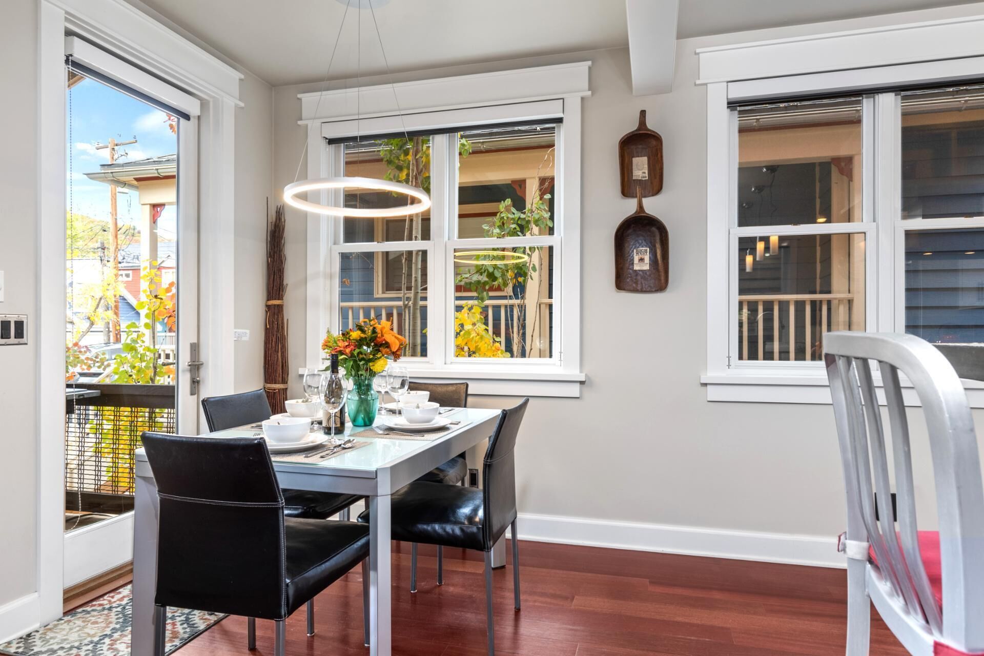 A dining area with a table set for four, two black chairs, a vase of flowers, and a hanging light fixture.