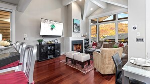 A spacious living room with a fireplace, a television, and a large window offering a view of autumn foliage. - Red Crest 3 Bedrooms PWS-957 by KBM (Park City)