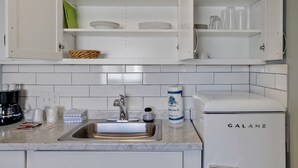 Une cuisine avec des meubles blancs, un évier, une machine à café et un réfrig érateur de la marque Galanz.