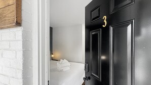 Une pièce avec un lit, une porte noire portant le numéro 3 et un mur en briques blanches.
