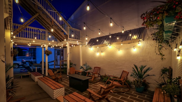 Un espace extérieur aménagé en terrasse, avec des bancs en bois, une table et des guirlandes lumineuses.