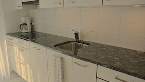 A modern kitchen with white cabinets, a granite countertop, a built-in sink, and a coffee maker. - Nest - Lauriedstrasse 9 (Zug)