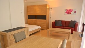 A modern, well-lit room with a wooden bed, a red sofa, a wooden dining table, and a large wardrobe. - Nest - Lauriedstrasse 9 (Zug)