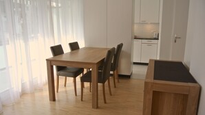 A dining area with a wooden table and chairs, a kitchen in the background, and a door to the right. - Nest - Lauriedstrasse 9 (Zug)