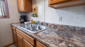 A kitchen with granite countertops, stainless steel sinks, wooden cabinets, and a coffee maker. - Cottage #3 Snow Day, 2 Bedroom Cottage (Lake City)