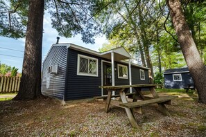 Een klein huisje met een veranda en een picknicktafel, omringd door bomen.