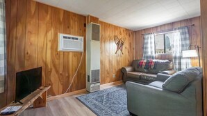 A living room with wooden walls, a sofa, a television on a stand, and a window with curtains. - Cottage #3 Snow Day, 2 Bedroom Cottage (Lake City)