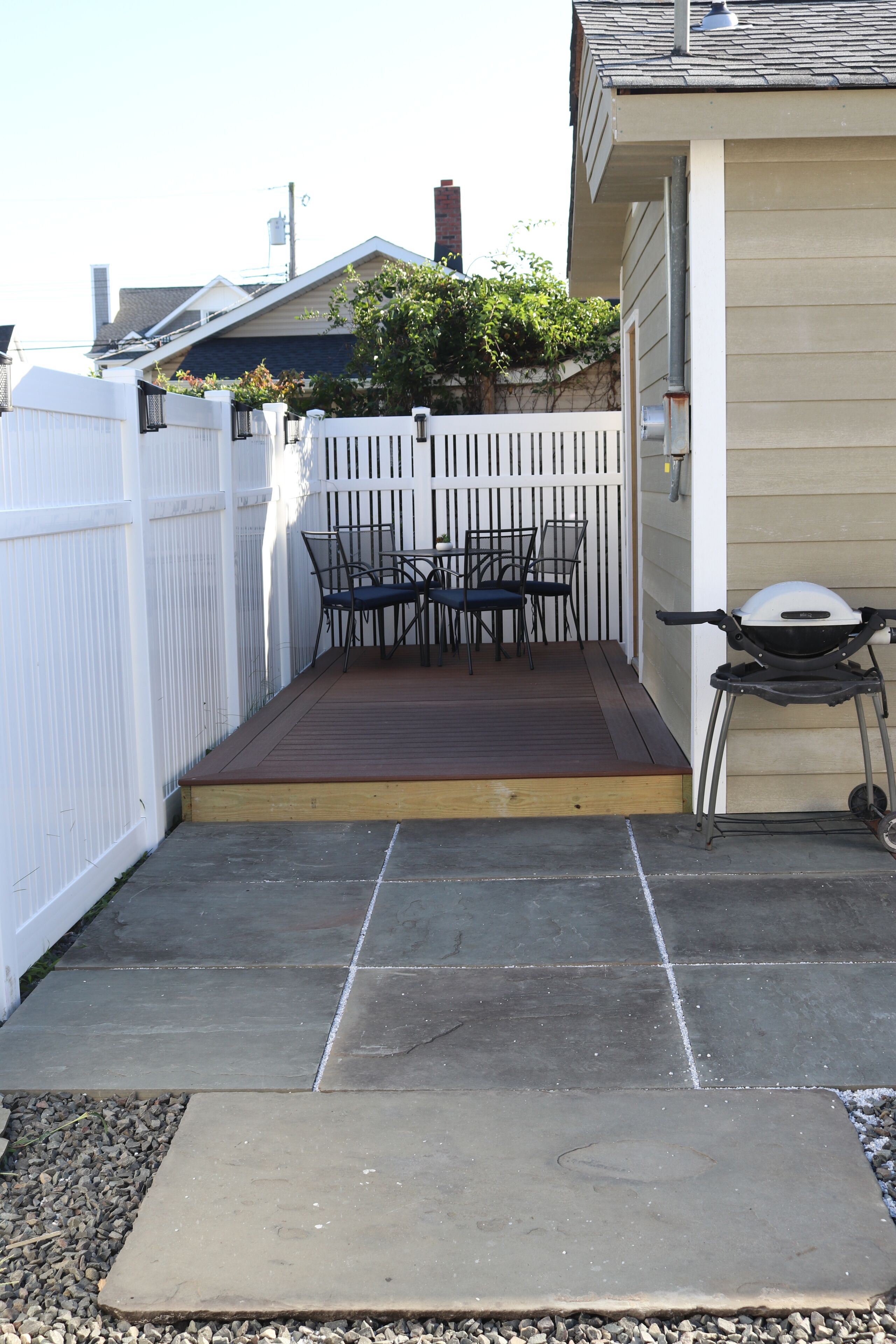 A patio with a wooden deck, a barbecue grill, and a table with chairs.