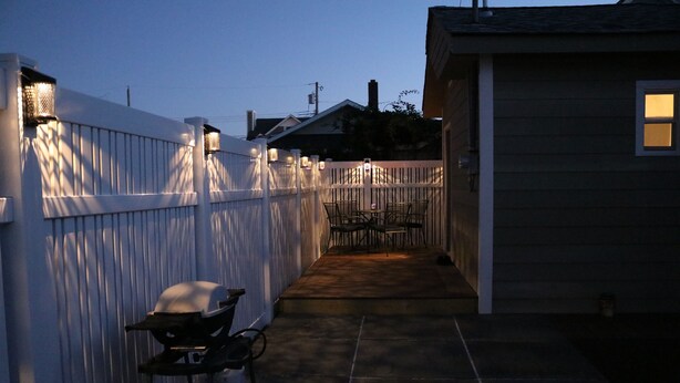 Un jardin avec un barbecue, une table de patio et une clôture blanche.