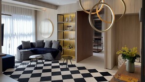 Ein modernes Wohnzimmer mit einem Schachbrettmuster-Boden, einer Couch mit Kissen, einem Couchtisch und einem Bücherregal mit Dekorationselementen.