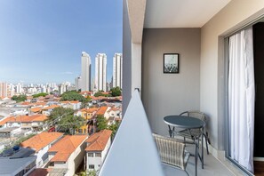 A balcony with a view of a cityscape, a table, and chairs. - Cyrela For You Carlos Petit (São Paulo)