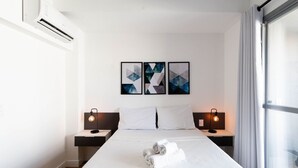 Ein Hotelzimmer mit einem großen Bett, zwei Nachttischen, einer Wand-Klimaanlage und einem Fenster mit Vorhängen.