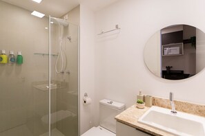 A modern bathroom with a glass-enclosed shower, a white sink, and a round mirror. - Cyrela For You Carlos Petit (São Paulo)