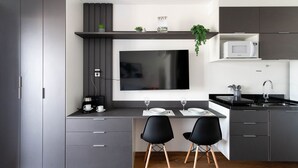 Eine moderne Küche mit integriertem Fernseher, grauen Schränken, einer schwarzen Arbeitsplatte und zwei schwarzen Stühlen.