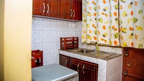 A compact kitchen with wooden cabinets, a marble backsplash, a sink, and a small refrigerator. - Beautiful 2-bed House in Kampala (Kampala)