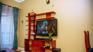 A living room with a TV mounted on a wooden entertainment unit, a red chair, and a potted plant. - Beautiful 2-bed House in Kampala (Kampala)