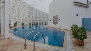 A swimming pool with a white tiled deck, surrounded by a white building with a grid-like facade. - Nasma Holiday Homes - Jumeirah Bay X1 To (Dubai)