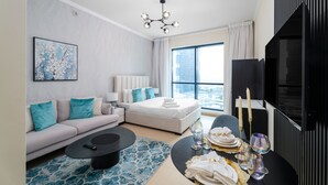 A modern hotel room with a sofa, a dining table set for two, a large window with a city view, and a flat-screen TV. - Nasma Holiday Homes - Jumeirah Bay X1 To (Dubai)