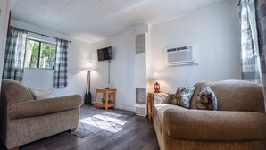 Ein Zimmer mit zwei Sofas, einem Fernseher, einer Klimaanlage und einem Fenster mit Vorhängen.