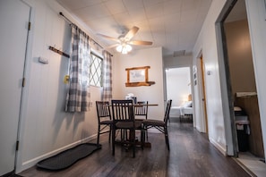 A room with a dining table, chairs, a ceiling fan, a window with curtains, a door, and a small rug.
