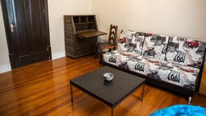 Un salón con suelo de madera, un sofá estampado con motivos de la Ruta 66, un mueble de madera y una mesa de centro negra.