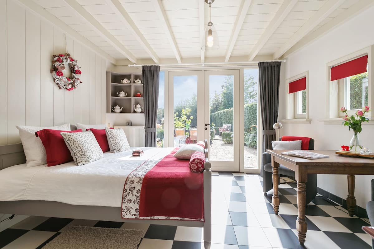 Ein Schlafzimmer mit einem Bett, einem Tisch und Blick auf den Garten durch eine Glastür.