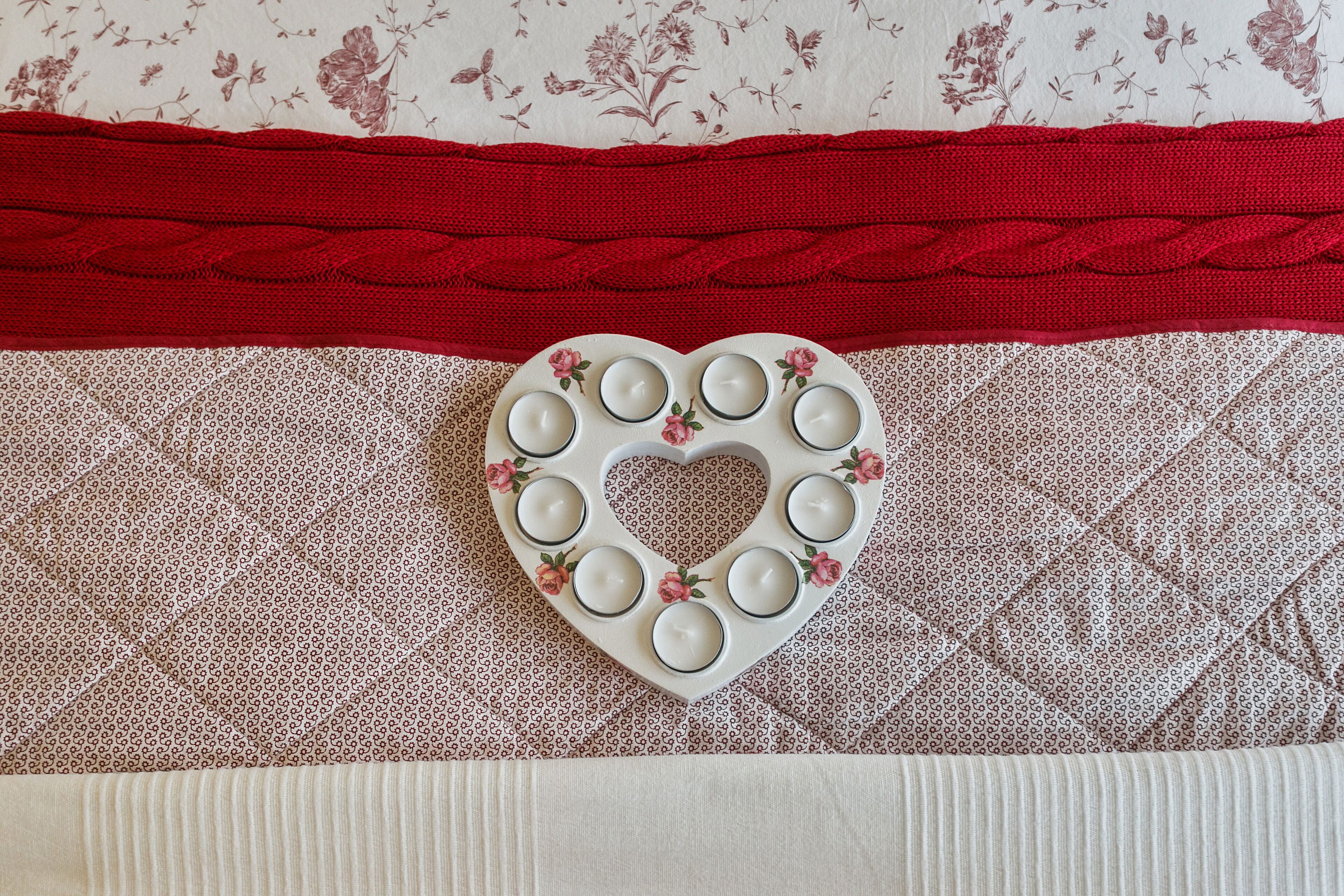 A heart-shaped candle holder with candles on a patterned fabric surface.