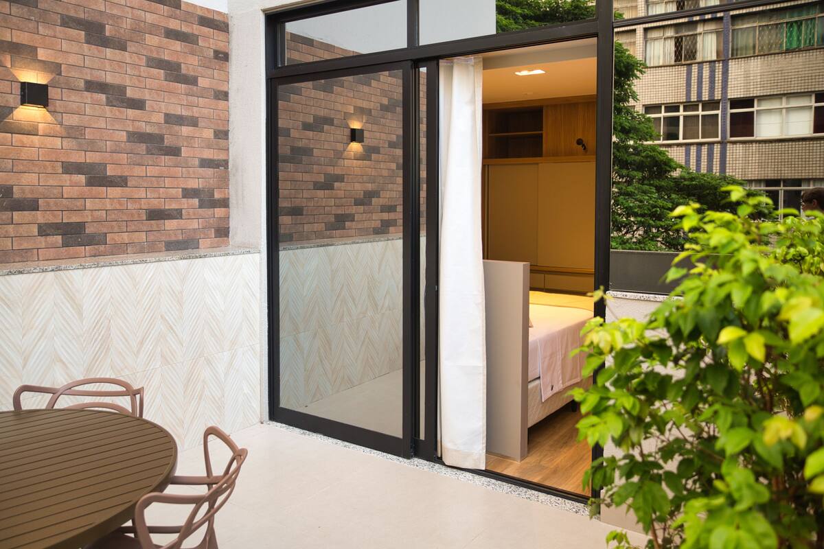 A modern hotel room with a sliding glass door leading to a balcony, a wooden table, and chairs outside.