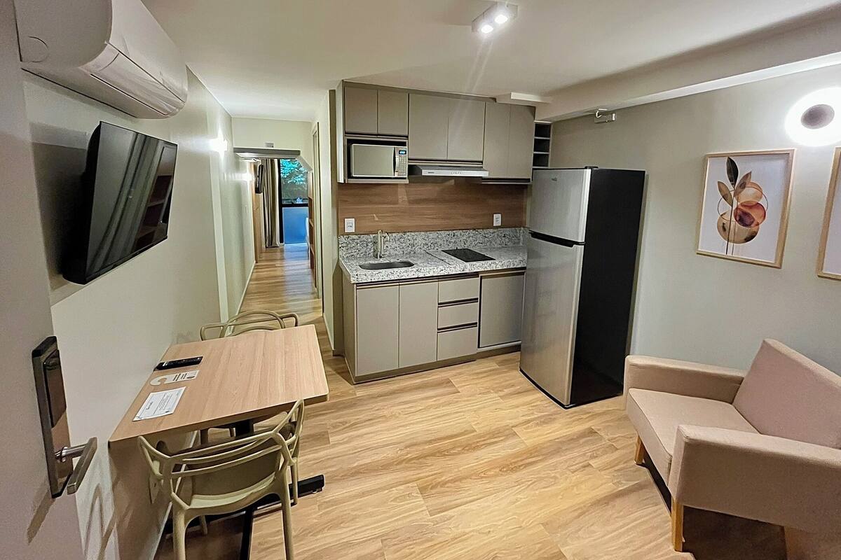 A compact kitchen with a microwave, refrigerator, and granite countertop. There is a dining table with chairs and a sofa in the living area.