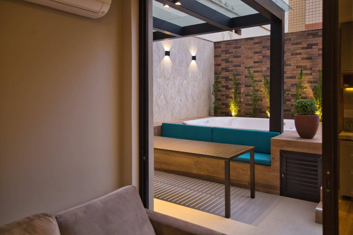 An outdoor seating area with a wooden table and benches, a brick wall, and a potted plant.