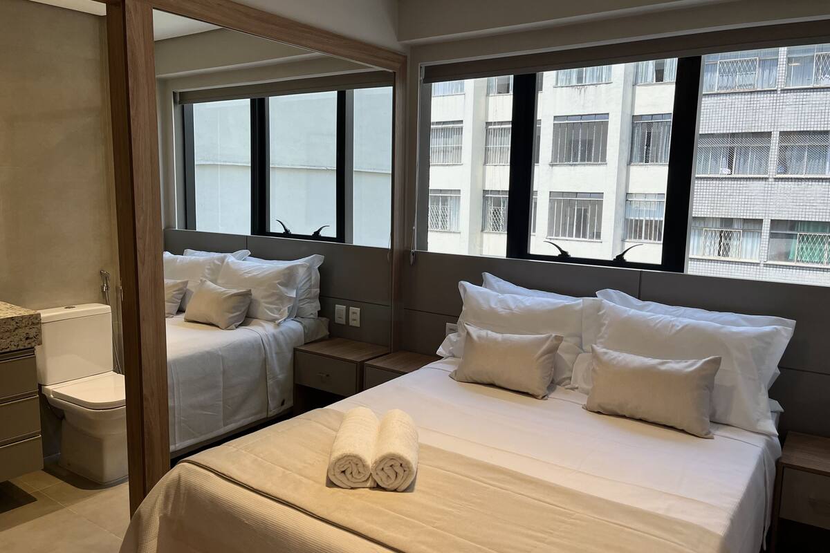 A hotel room with a bed, a bathroom, and a large window.