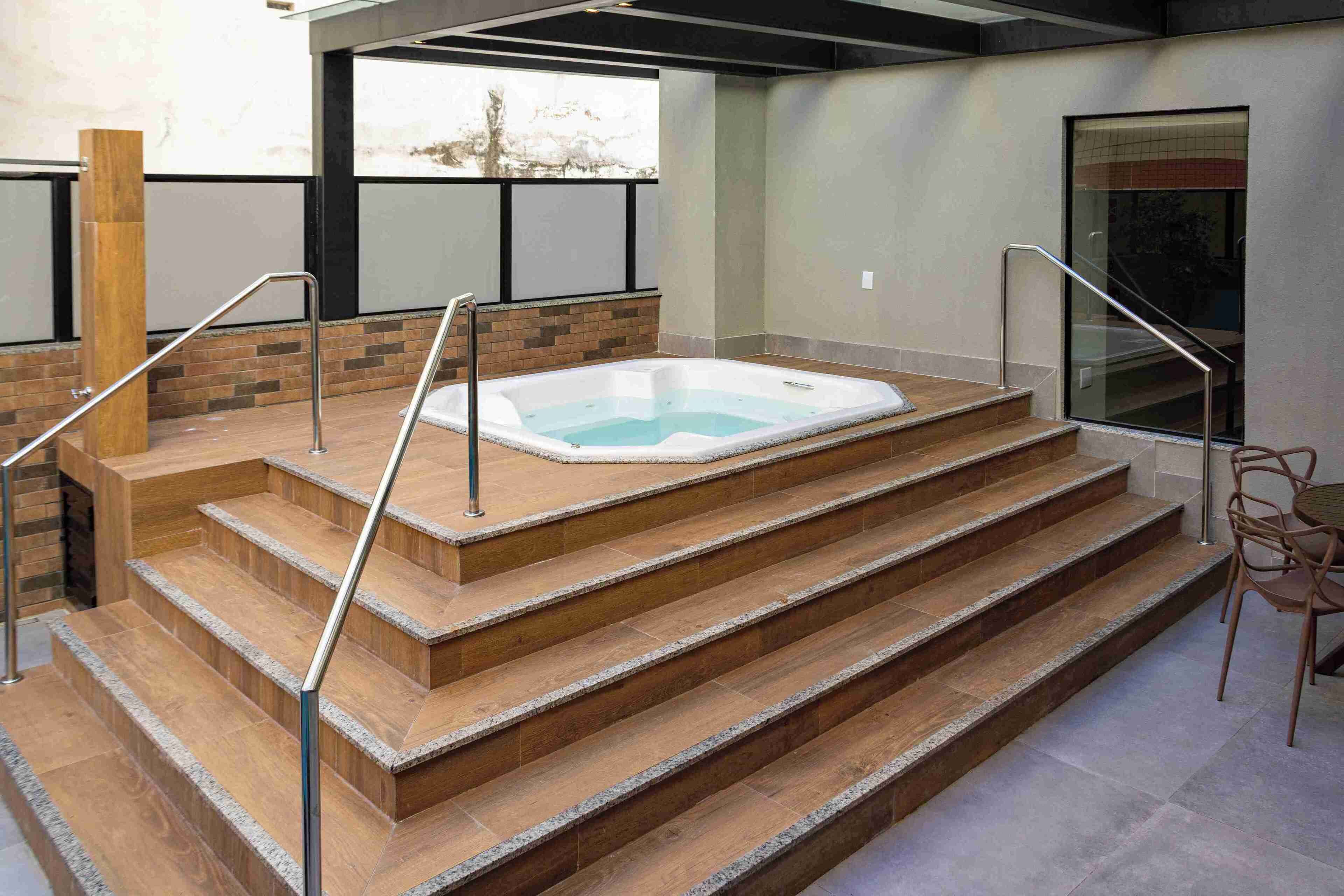 Uma área moderna de piscina interna com hidromassagem, escadas de madeira e grades de metal.