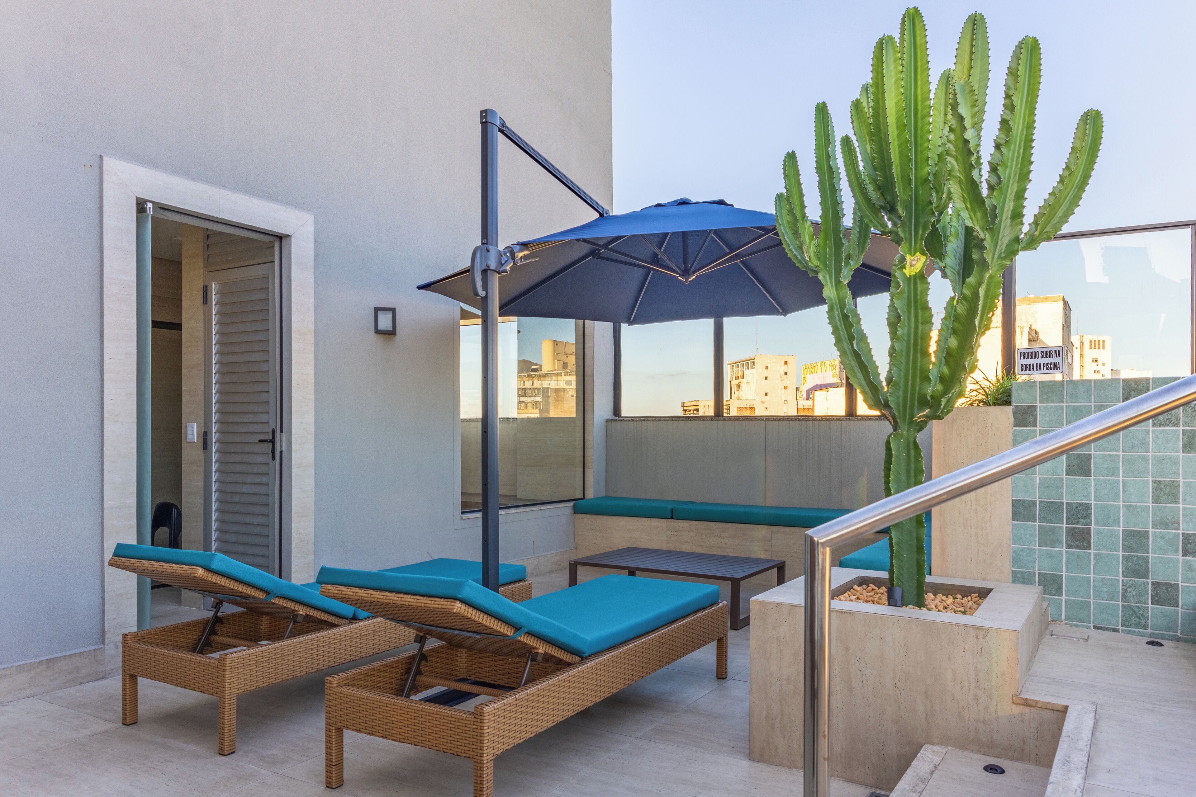 Una terraza en la azotea con sillones de mimbre, un parasol azul y una gran planta de cactus.