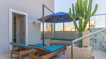 Una terraza en la azotea con sillones de mimbre, un parasol azul y una gran planta de cactus.