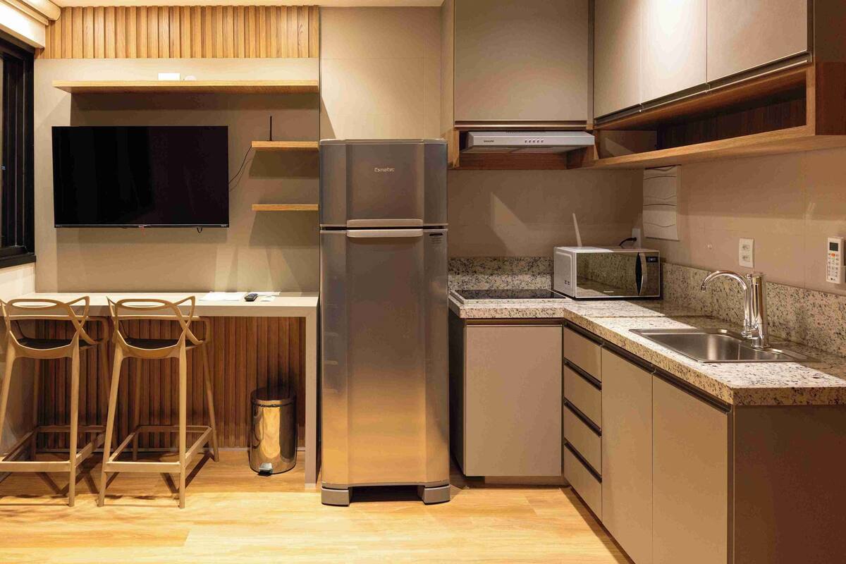 A compact kitchen with a refrigerator, microwave, and a TV mounted on the wall.
