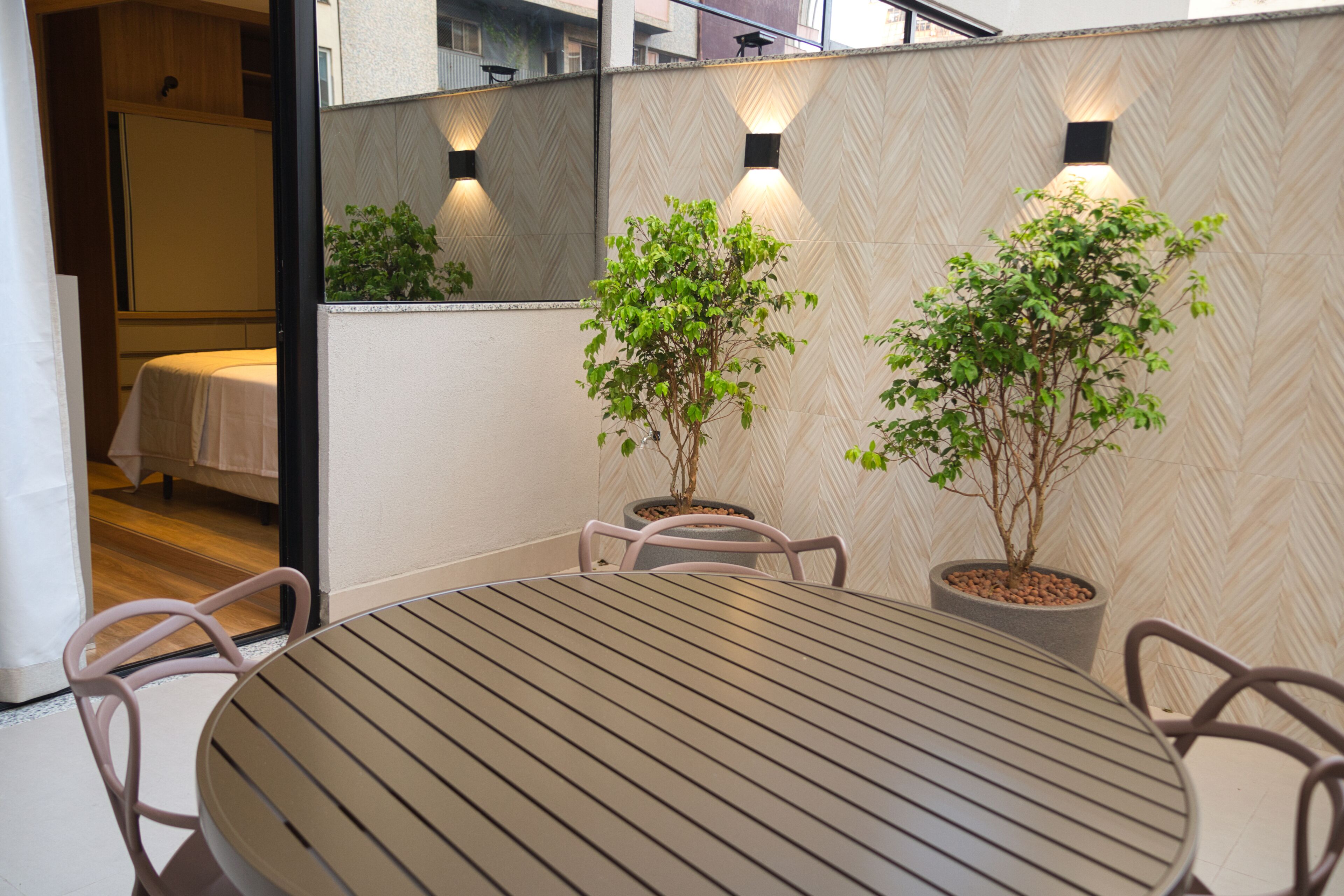 Une table ronde entourée de chaises en métal, deux plantes en pot et un mur orné d’un motif en chevrons, agrémenté de luminaires fixés au mur.