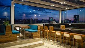 A modern rooftop bar with a city view, featuring wooden furniture and a glass railing. - Life Residence (Belo Horizonte)