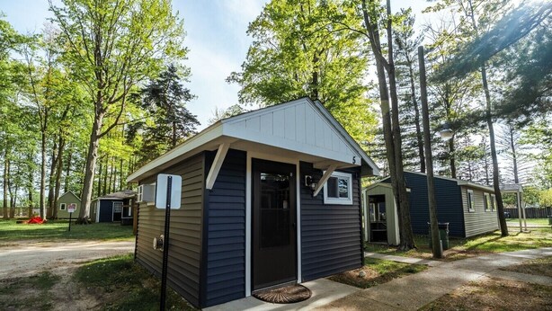 A small, single-story cabin with a front door and a small porch, surrounded by trees.