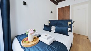 Ein Hotelzimmer mit einem Bett, einem Holz-Kopfteil, einem Nachttisch mit Obstschale und Blumenvase sowie einer Tür.